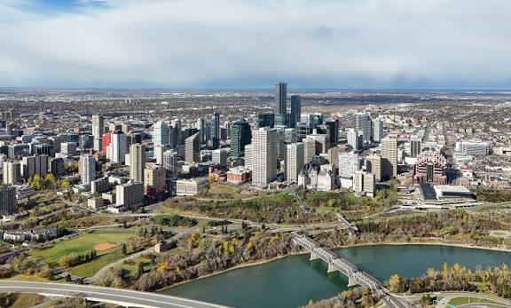 Aerial view of downtown Edmonton, Alberta, featuring the city skyline, high-rise buildings, the North Saskatchewan River, and bridges surrounded by green parkland.